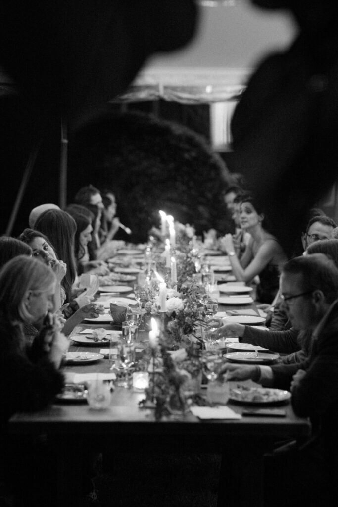 Long candlelit table during a wedding reception under tent.