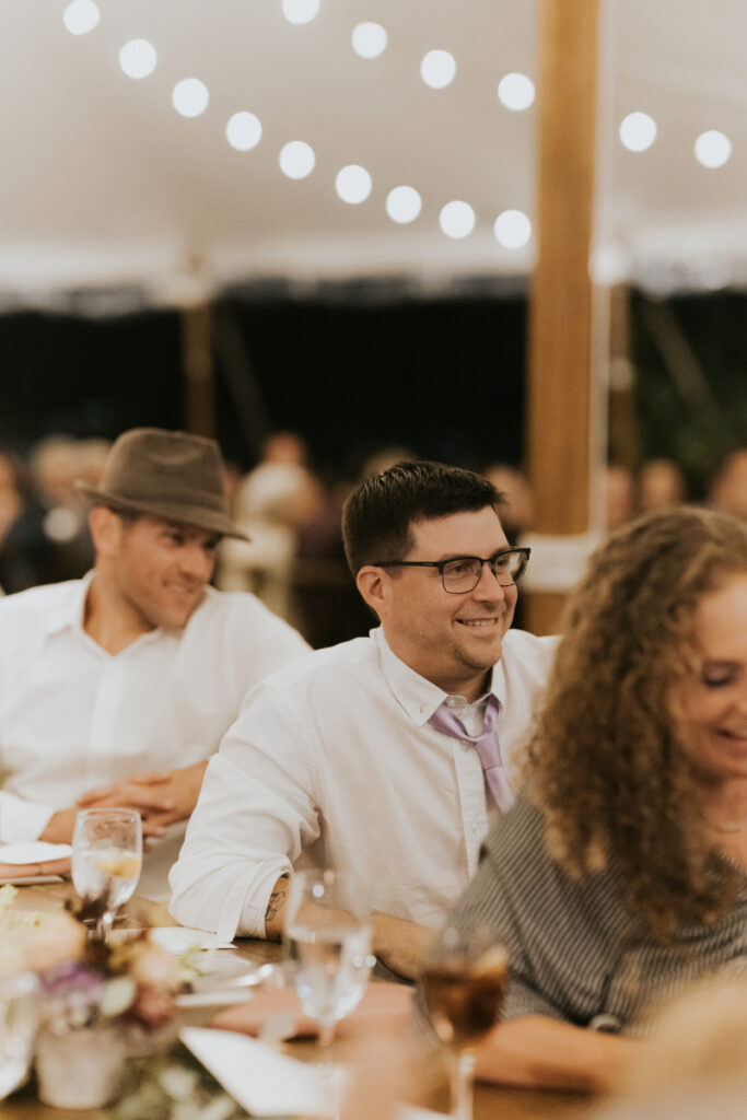 Guests laughing under string lights at Italian countryside wedding reception.