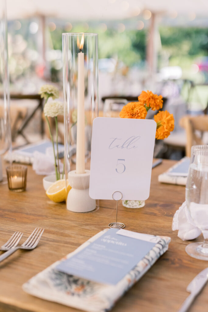 Reception table with table number, citrus details, taper candle, and floral menu setting.