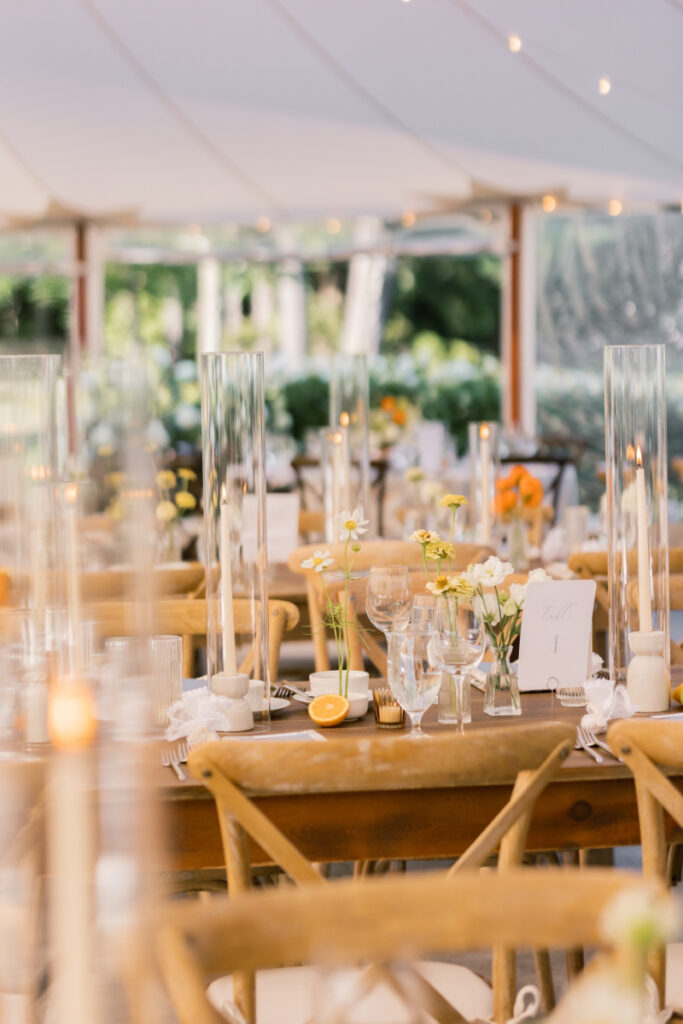 Reception tables decorated with citrus, florals, and tall glass candle holders under a sailcloth tent.