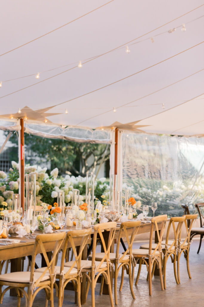 Reception tables decorated with citrus, florals, and tall glass candle holders under a sailcloth tent.