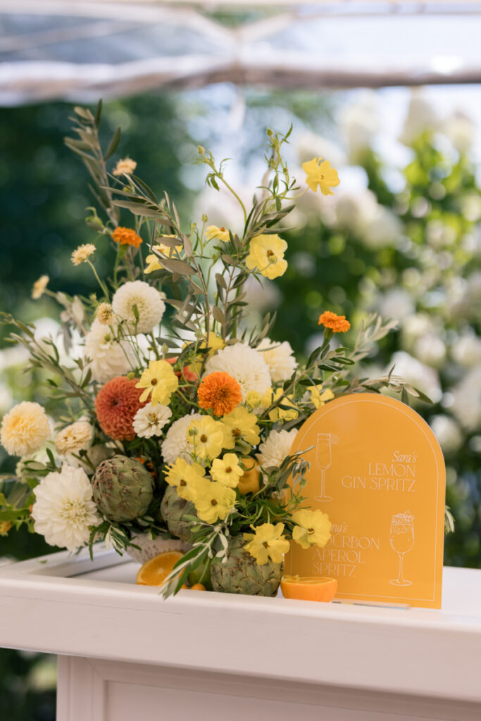 Citrus-toned signature drink sign and floral arrangement at a summer wedding at Connemara House.