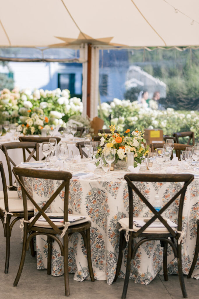 Close-up of place setting with floral napkin, blue menu card, and favor on a wooden table.