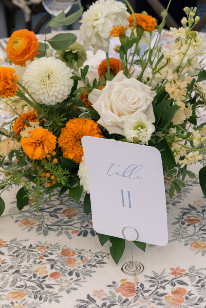 Minimalist bud vase with white cosmos flower on a wooden reception table with textured glassware.