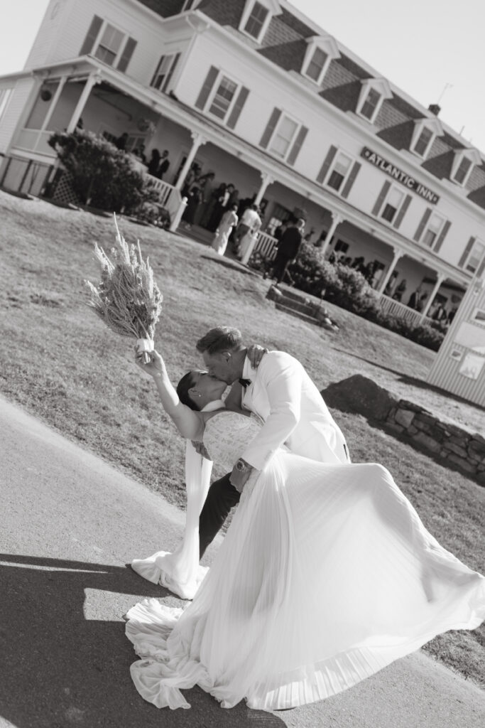Bride and groom share a dramatic dip kiss while holding bouquet outside a Block Island Wedding