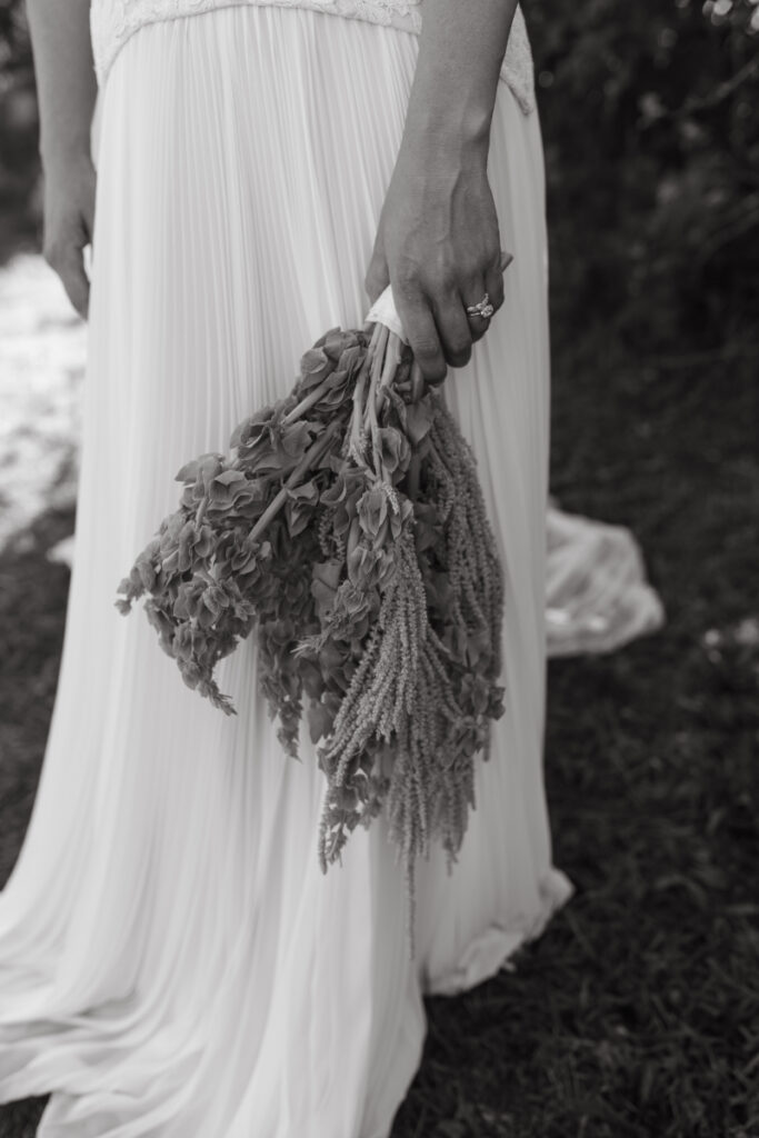 Bride holding cascading greenery bouquet beside flowing pleated wedding dress at a Block Island Wedding