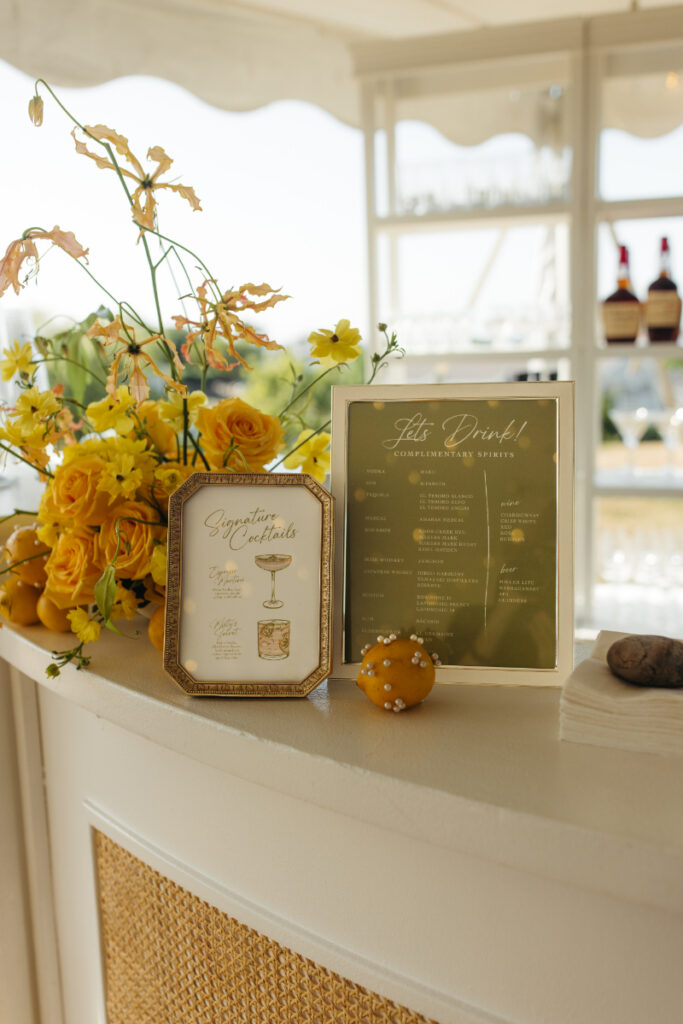Cocktail menu and yellow floral arrangement displayed on elegant reception bar.