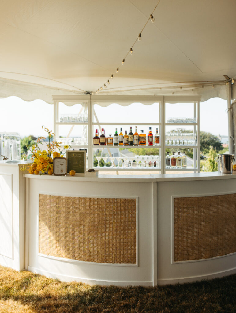 Wide view of reception bar under tent with liquor display and warm evening light.