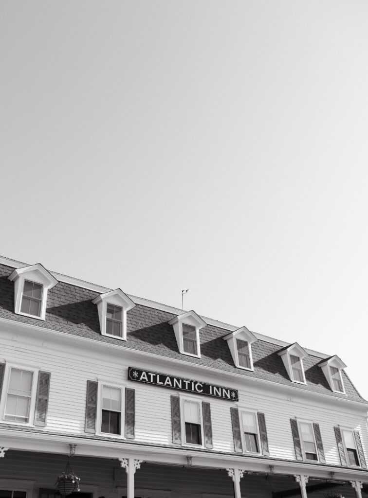 Exterior view of historic Atlantic Inn building overlooking lawn during seaside wedding celebration.