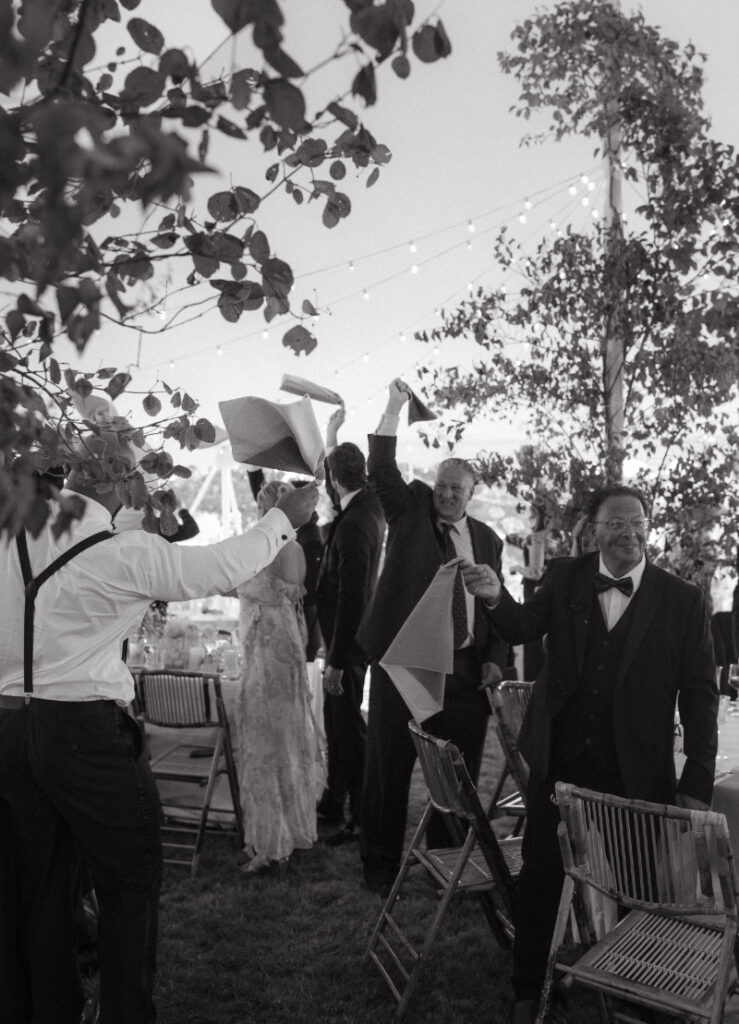 Guests cheering and waving napkins during energetic reception moment under string lights at a Block Island Wedding