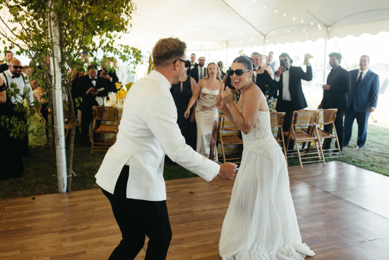 Bride wearing sunglasses laughing while dancing with groom during lively tented Block Island Wedding