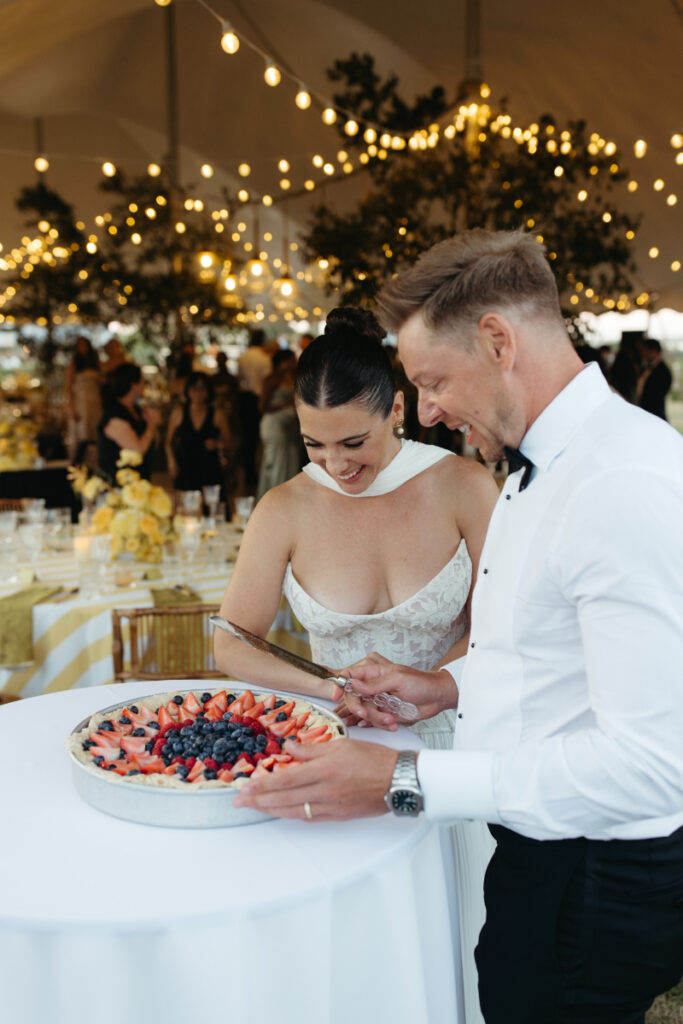 Bride and groom cutting berry-topped cake together during lively tented Block Island Wedding