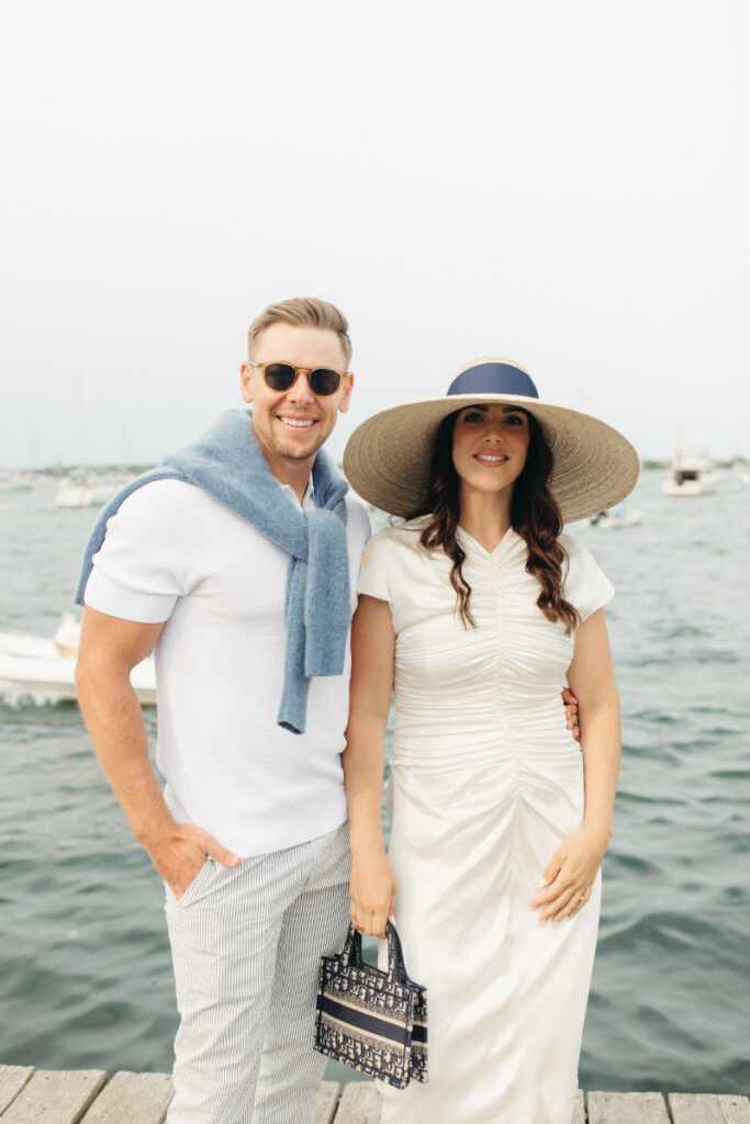 Couple standing by harbor in sun hats during relaxed welcome party for Block Island wedding weekend.