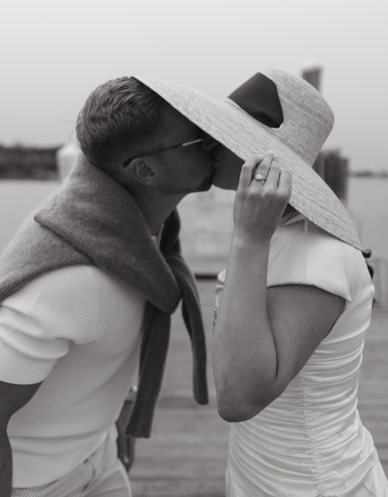 Couple kissing in sun hat and sweater during stylish welcome party at Block Island wedding weekend.