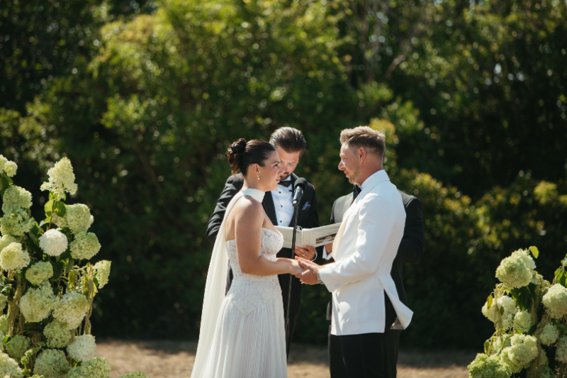Bride and groom holding hands while exchanging vows during outdoor ceremony.