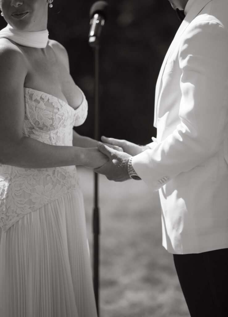 Close up of bride and groom holding hands during outdoor wedding ceremony.