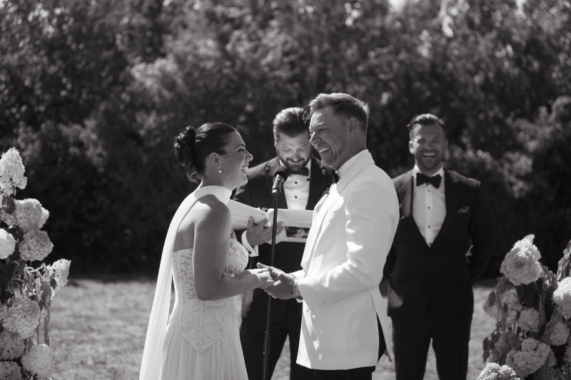 Bride and groom smiling and holding hands during joyful wedding ceremony moment.