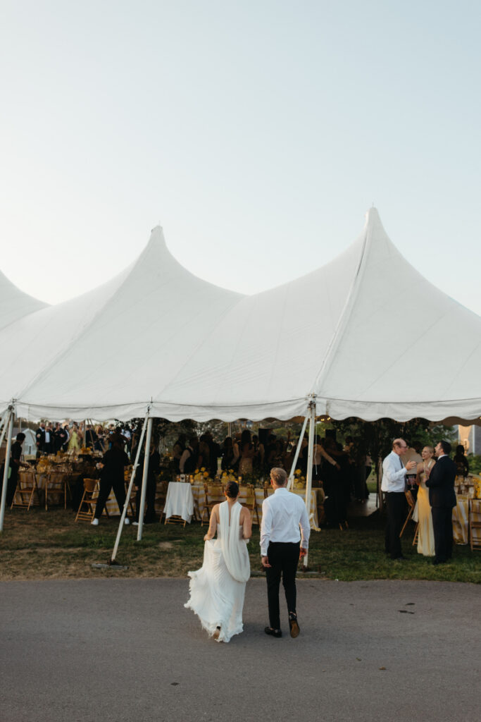 Bride and groom walking into reception tent as guests gather and evening celebration begins.