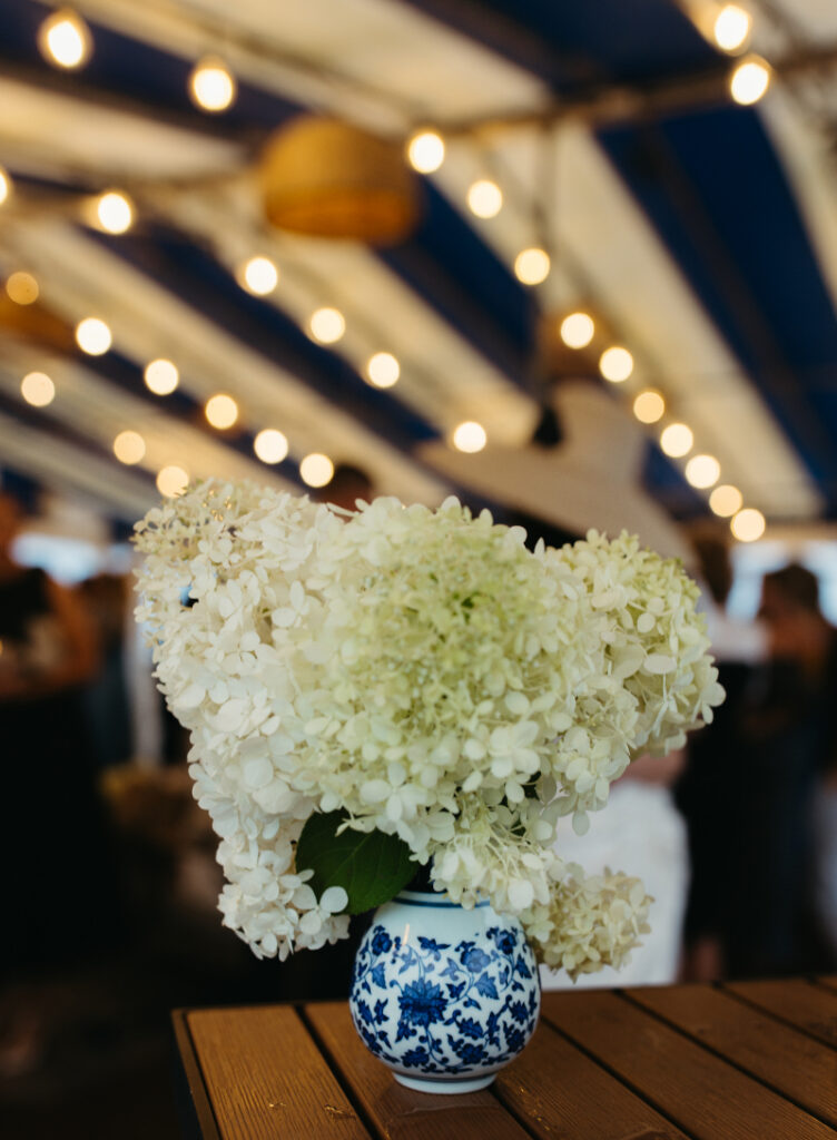 White hydrangea centerpiece in blue vase under tent lights during elegant Block Island wedding reception.