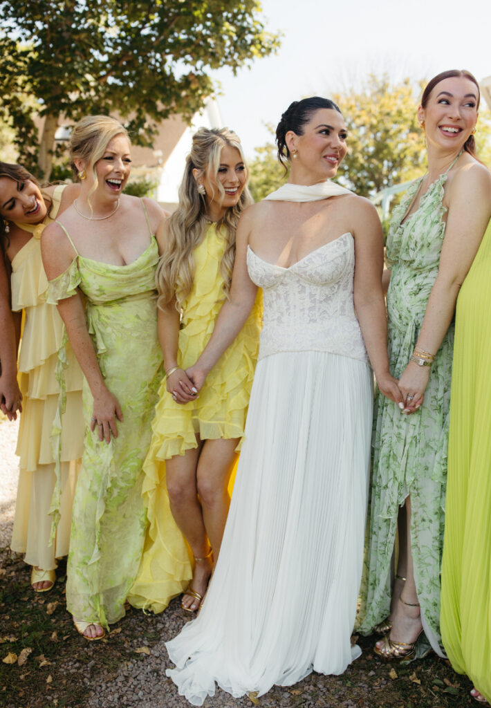 Bride laughing with bridesmaids in yellow and green dresses during joyful pre-ceremony portraits.