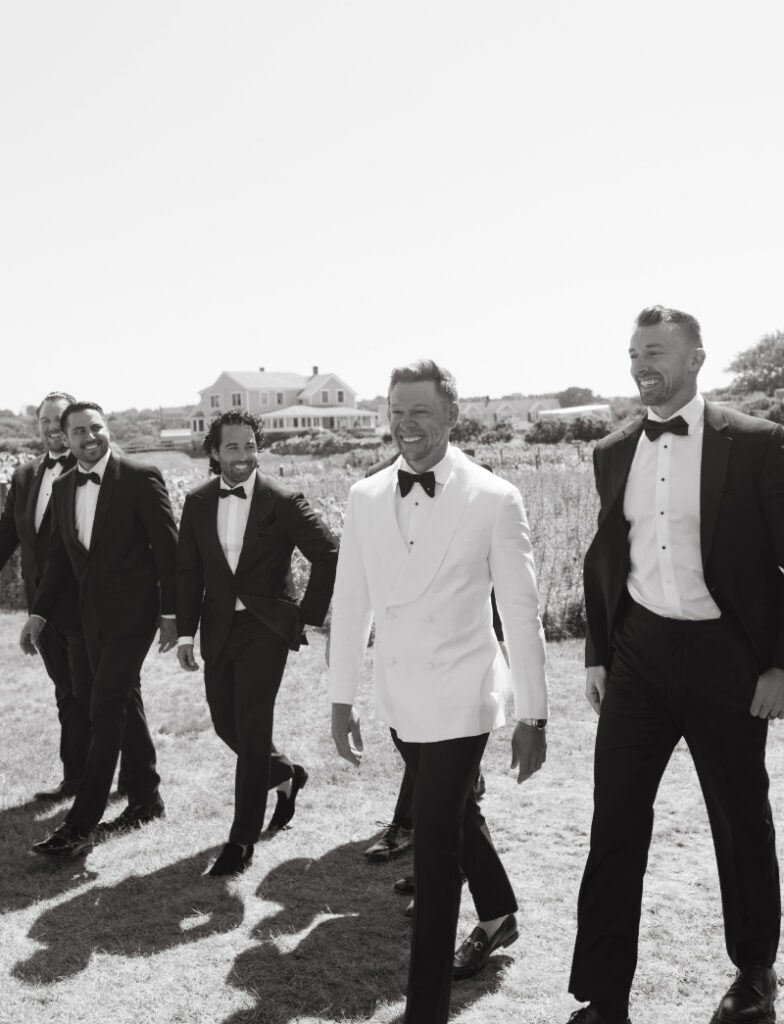Groom walking with groomsmen in tuxedos along coastal lawn before the Block Island Wedding