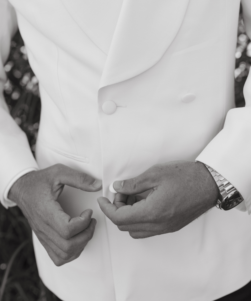 Groom buttoning white dinner jacket, capturing elegant wedding attire details.