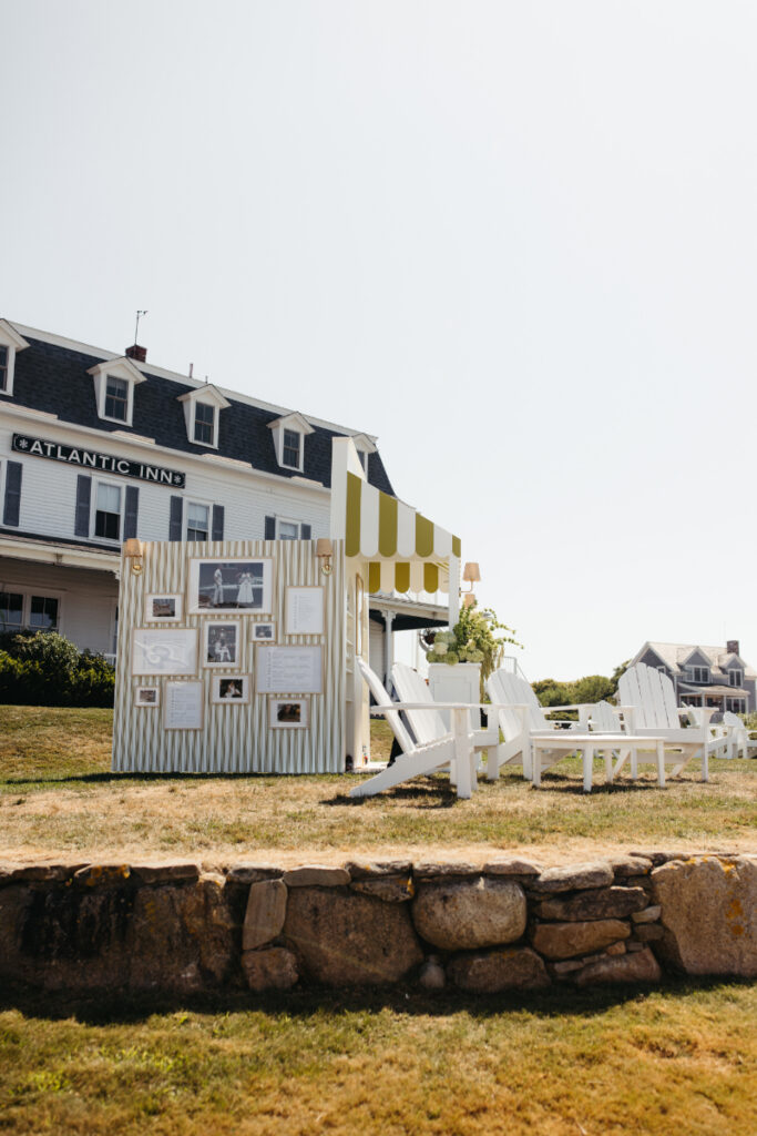 Striped photo display wall and lounge setup outside seaside wedding reception tent.