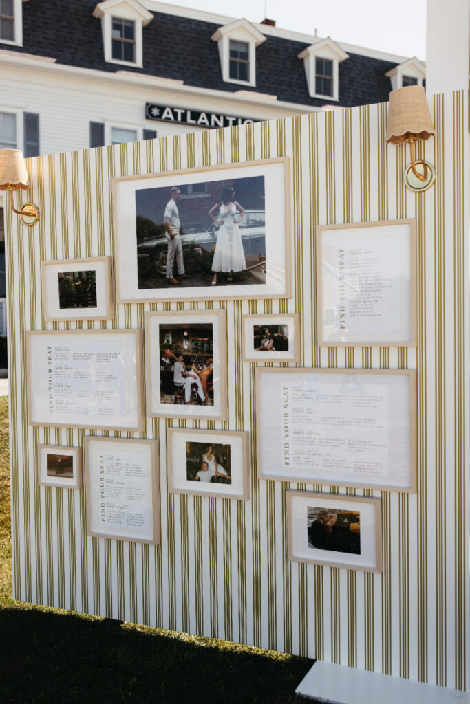 Striped display wall featuring framed photos and seating chart near outdoor cocktail hour lawn.