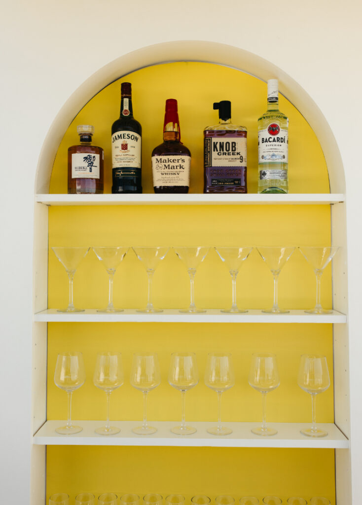 Back bar shelves with liquor bottles and martini glasses inside custom cocktail bar.