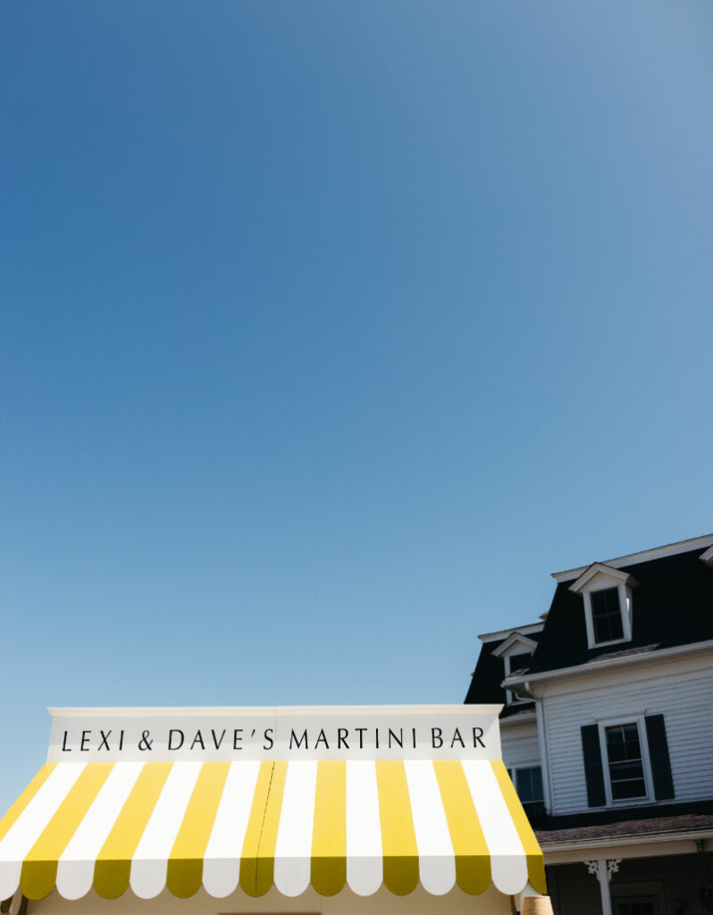 Yellow striped martini bar awning with clear blue sky above outdoor reception lawn.