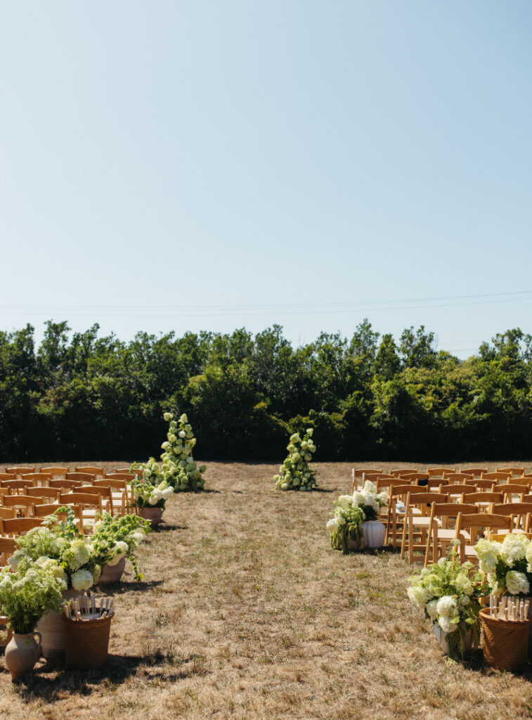 Outdoor ceremony aisle with wooden chairs and hydrangea florals during garden style Block Island wedding ceremony.