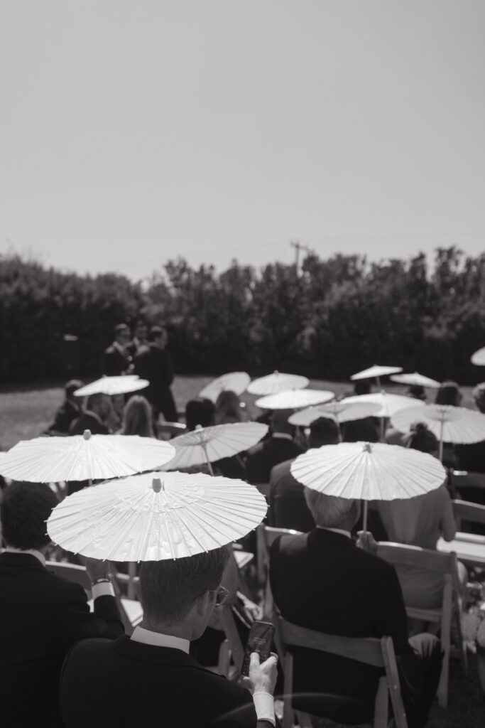 Guests seated with white parasols during outdoor ceremony at elegant summer Block Island wedding.