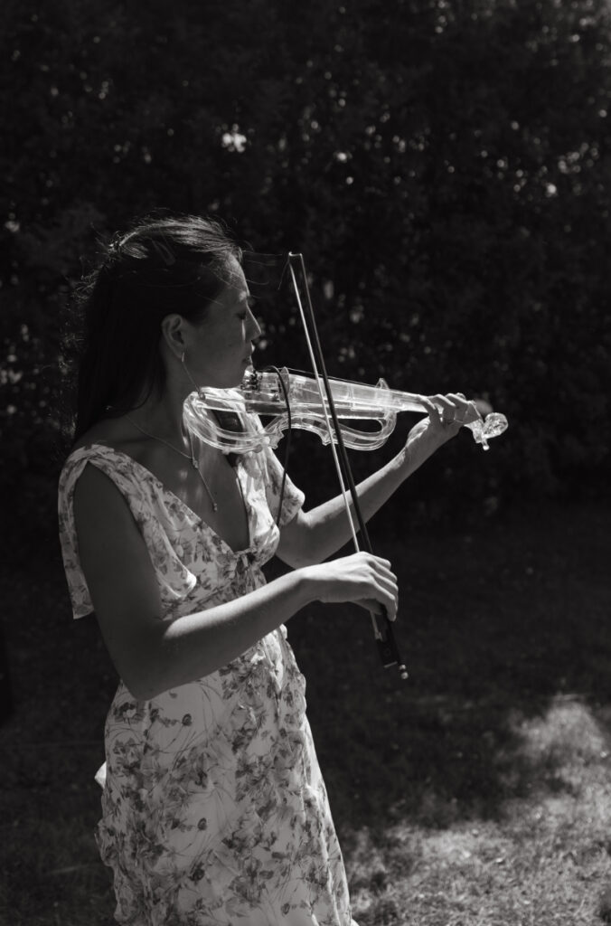 Violinist performing during cocktail hour outdoors as guests gather after ceremony.