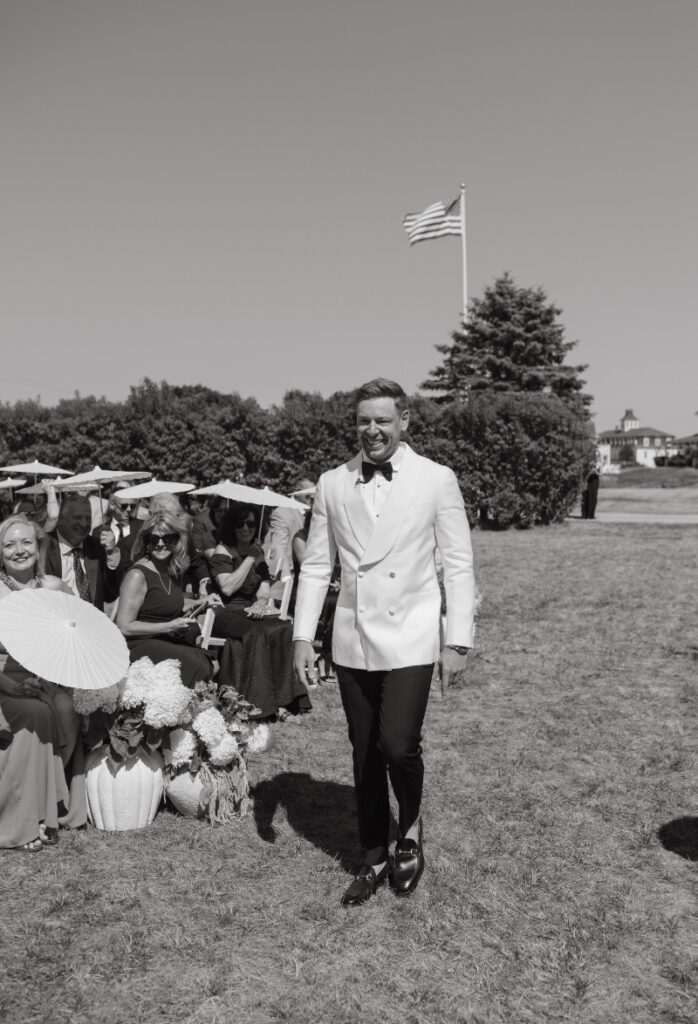 Groom walking down ceremony aisle past guests during outdoor coastal Block Island wedding.