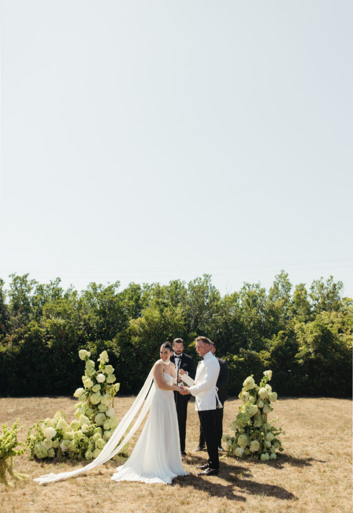 Bride and groom exchanging vows at floral ceremony arch during romantic outdoor Block Island wedding.