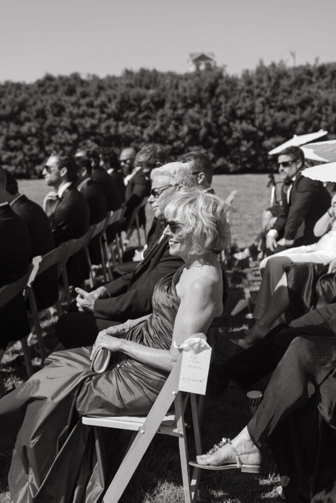 Guests seated during outdoor ceremony watching vows under bright sun.