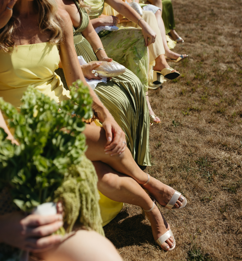 Guests in colorful dresses seated during ceremony holding shell purses.
