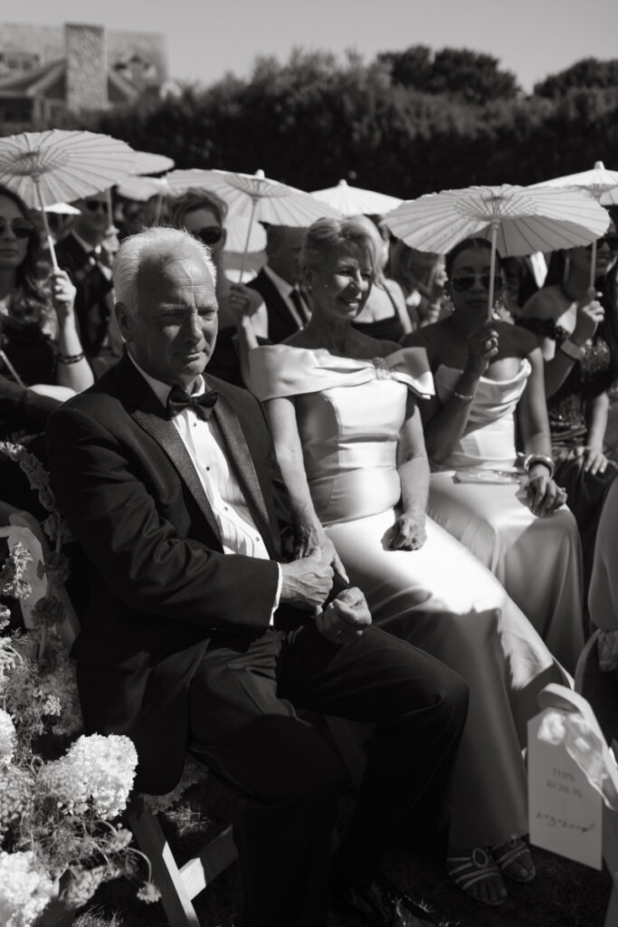 Family members seated together during ceremony holding white parasols.
