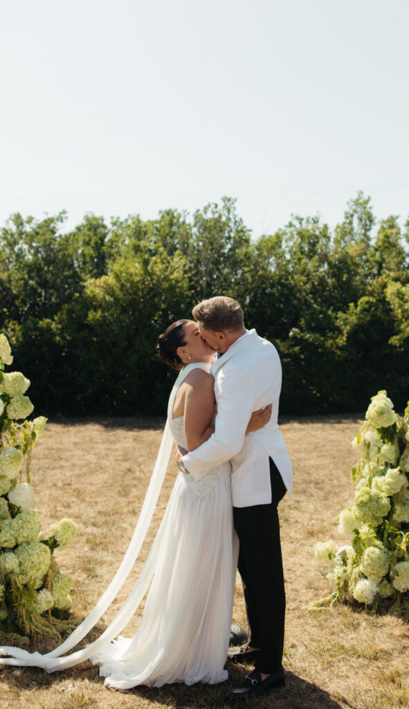 Bride and groom sharing a kiss beside floral ceremony arrangements.