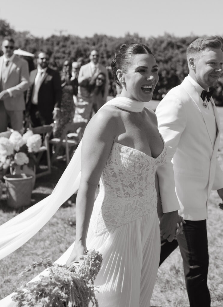 Bride smiling while walking down aisle with groom after ceremony.