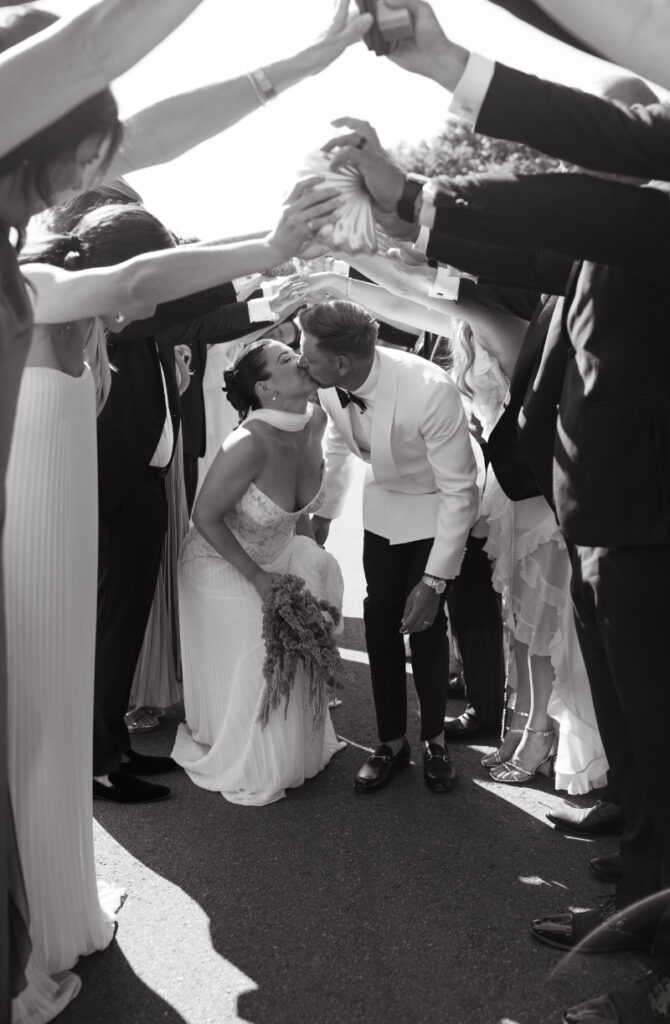 Guests spraying champagne while newlyweds kiss during joyful wedding celebration exit.