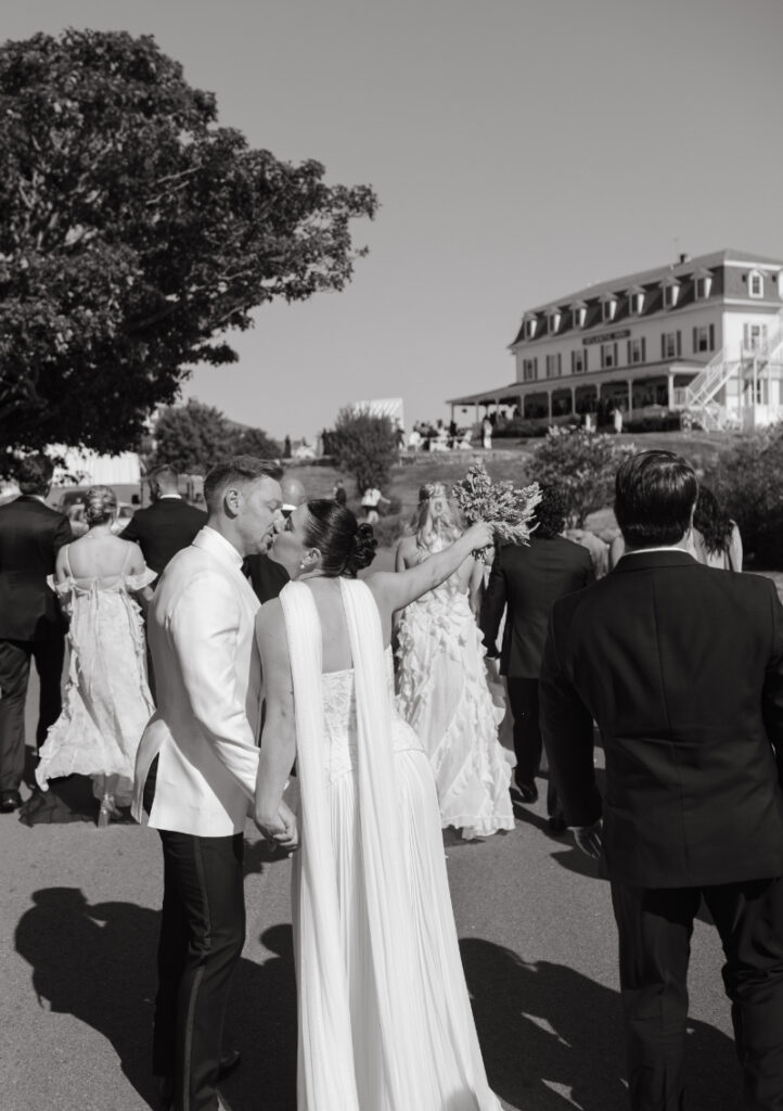 Bride and groom celebrating with guests gathered outside seaside wedding venue.
