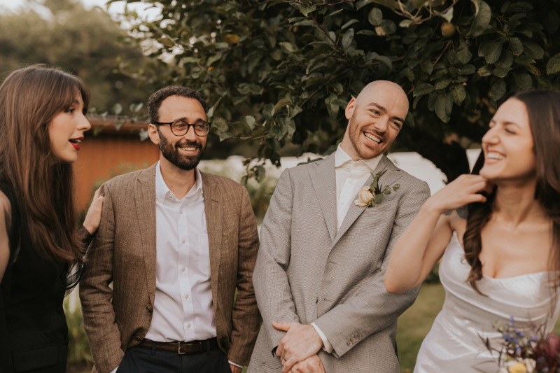 Two men smiling outdoors, one in brown blazer, one in light gray suit.