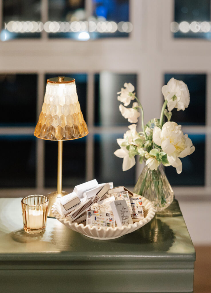 Green bar surface styled with a white dish of matchbooks, a votive candle, and a small vase of white flowers