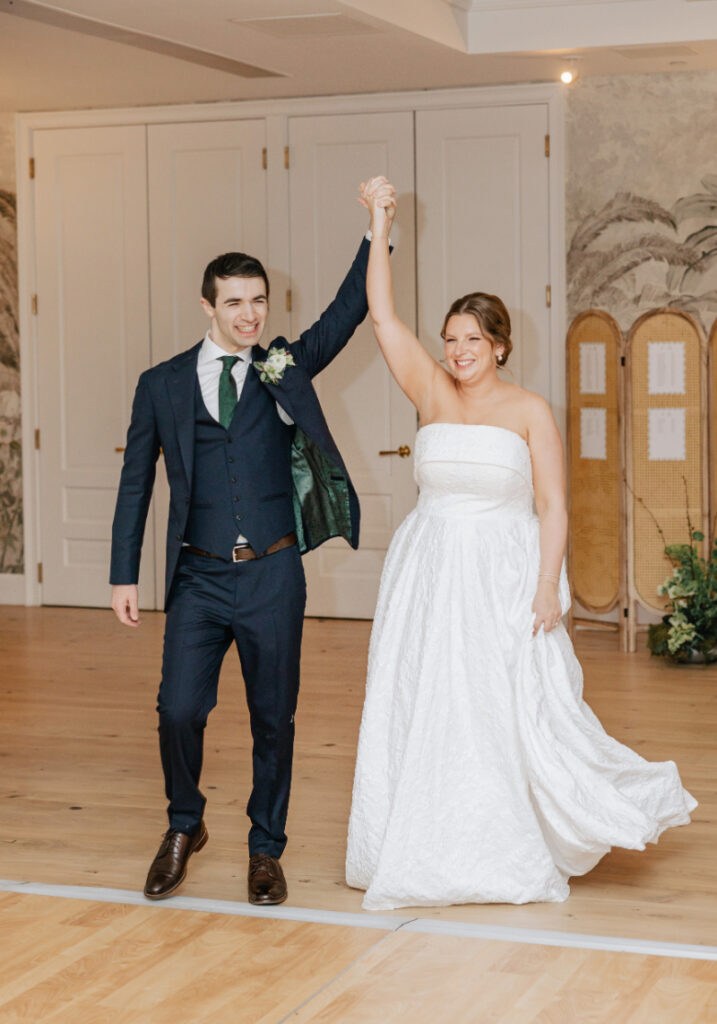 Couple entering the reception space with hands raised, smiling and celebrating