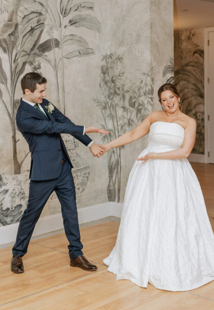 Couple dancing together, holding hands and laughing in front of a mural backdrop