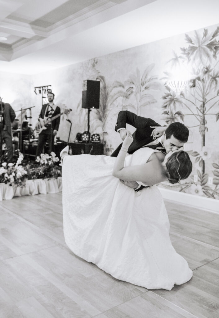 Couple performing a dip on the dance floor during their first dance with band in the background