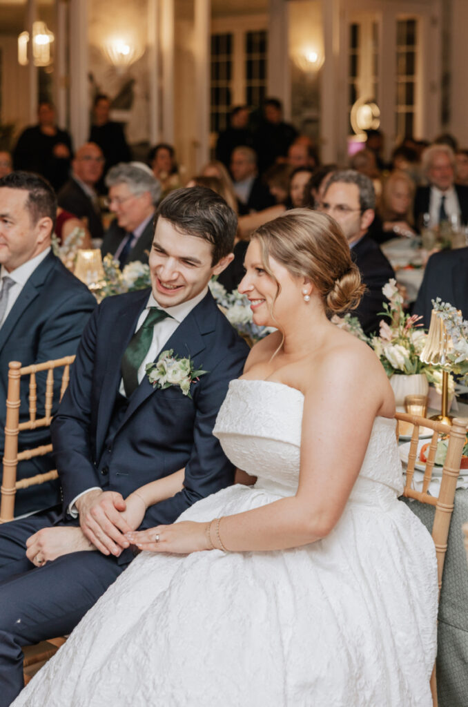 Couple seated at their reception table smiling and reacting during speeches