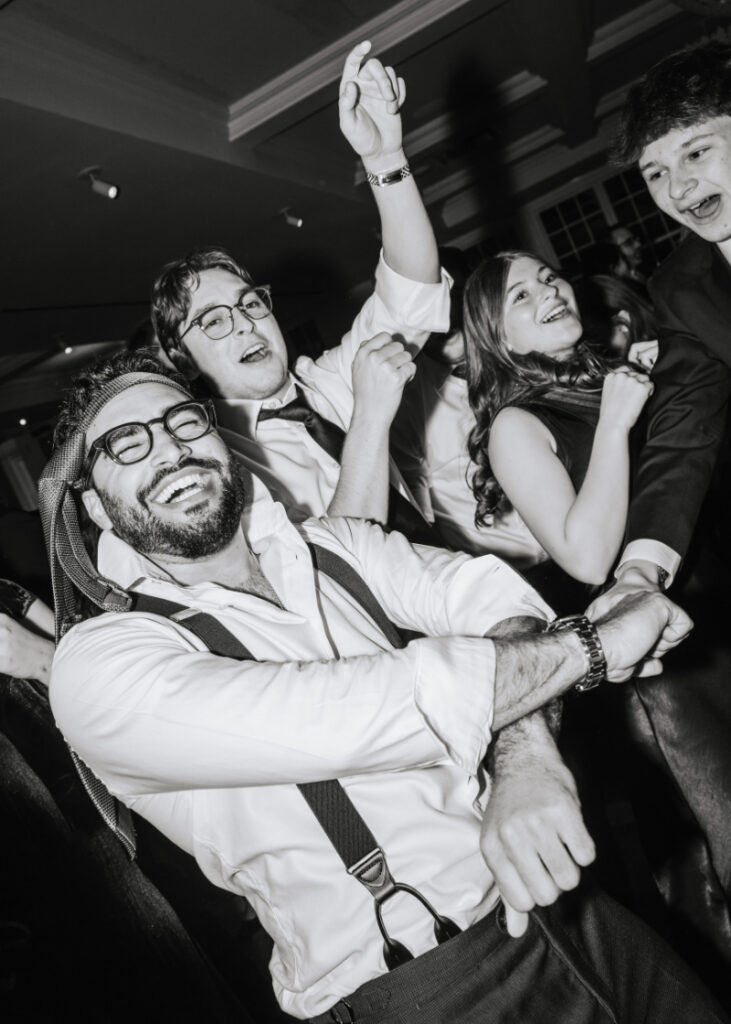 Group of guests dancing energetically with arms raised during the reception