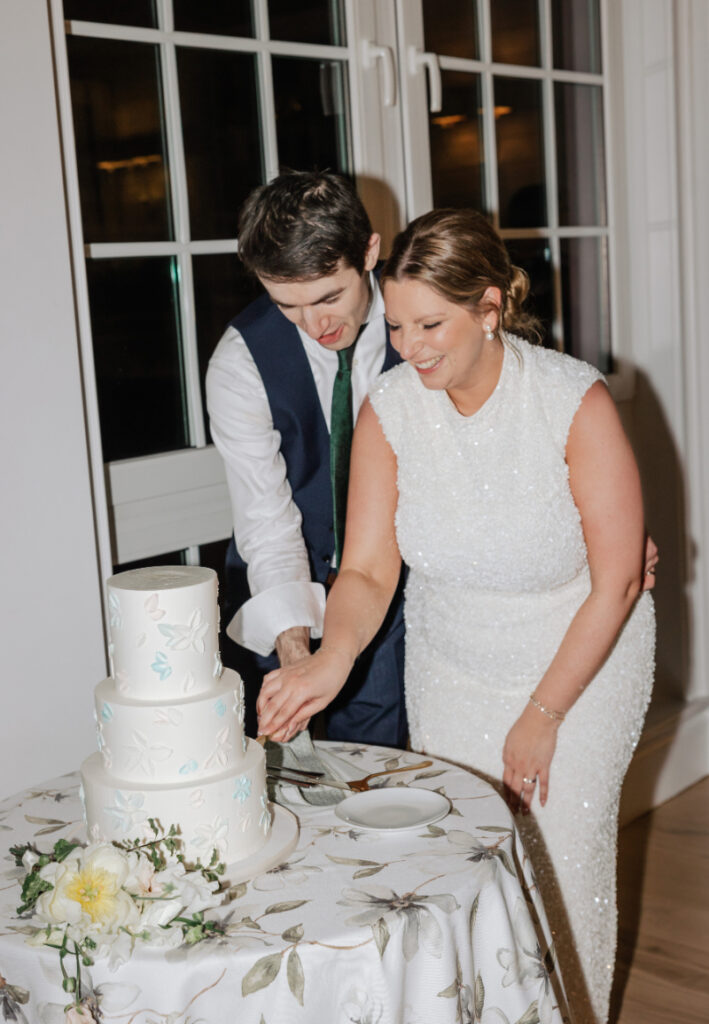 Couple cutting their wedding cake together at a decorated table near a window